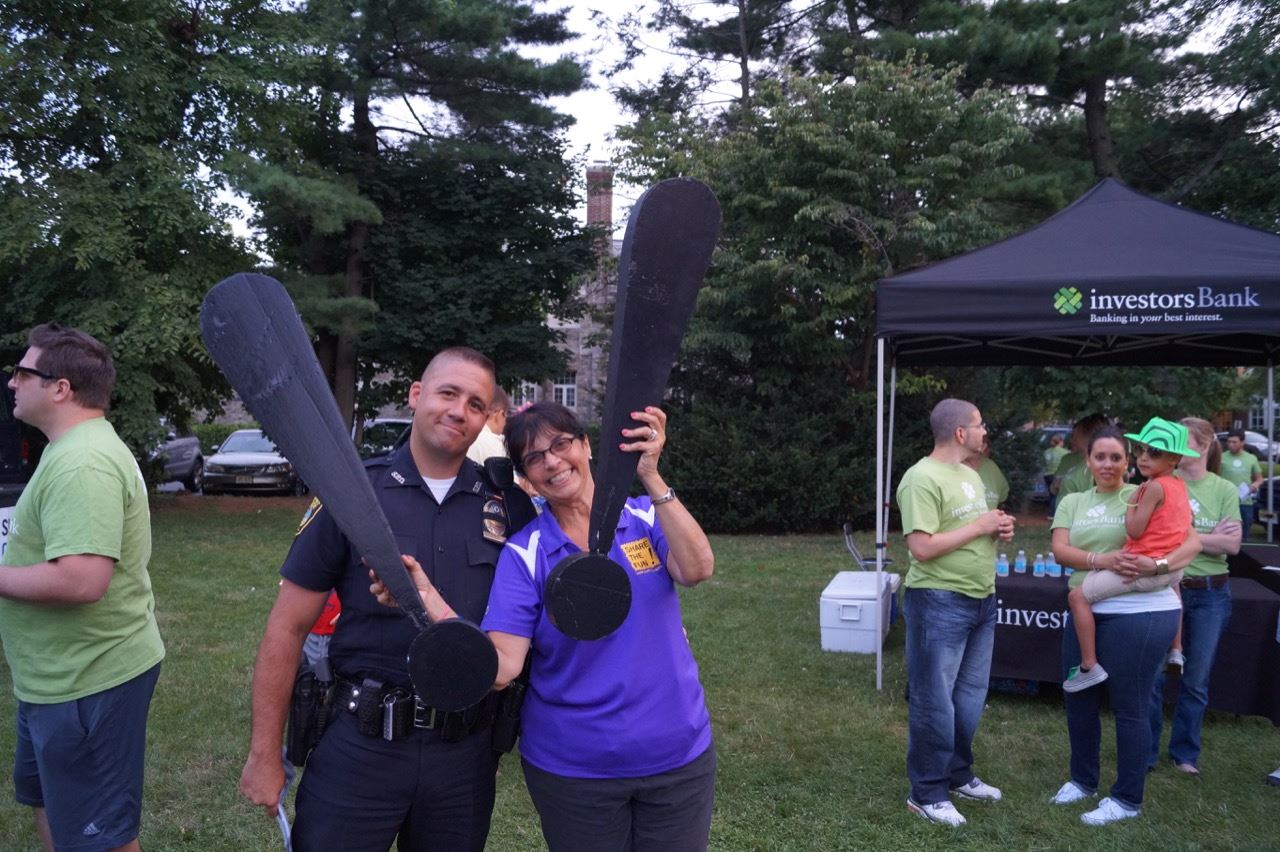 A Share the Fun representative holds the Share the Fun exclamation points next to a Police Officer.